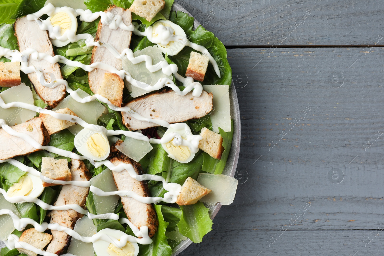 Photo of Delicious Caesar salad with chicken on grey wooden table, top view. Space for text