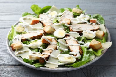 Photo of Delicious Caesar salad with chicken on grey wooden table, closeup