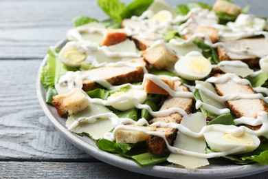 Photo of Delicious Caesar salad with chicken on grey wooden table, closeup