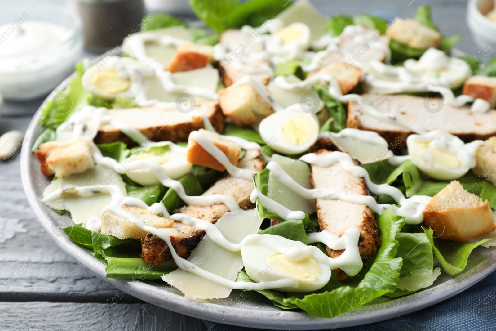 Photo of Delicious Caesar salad with chicken on grey wooden table, closeup