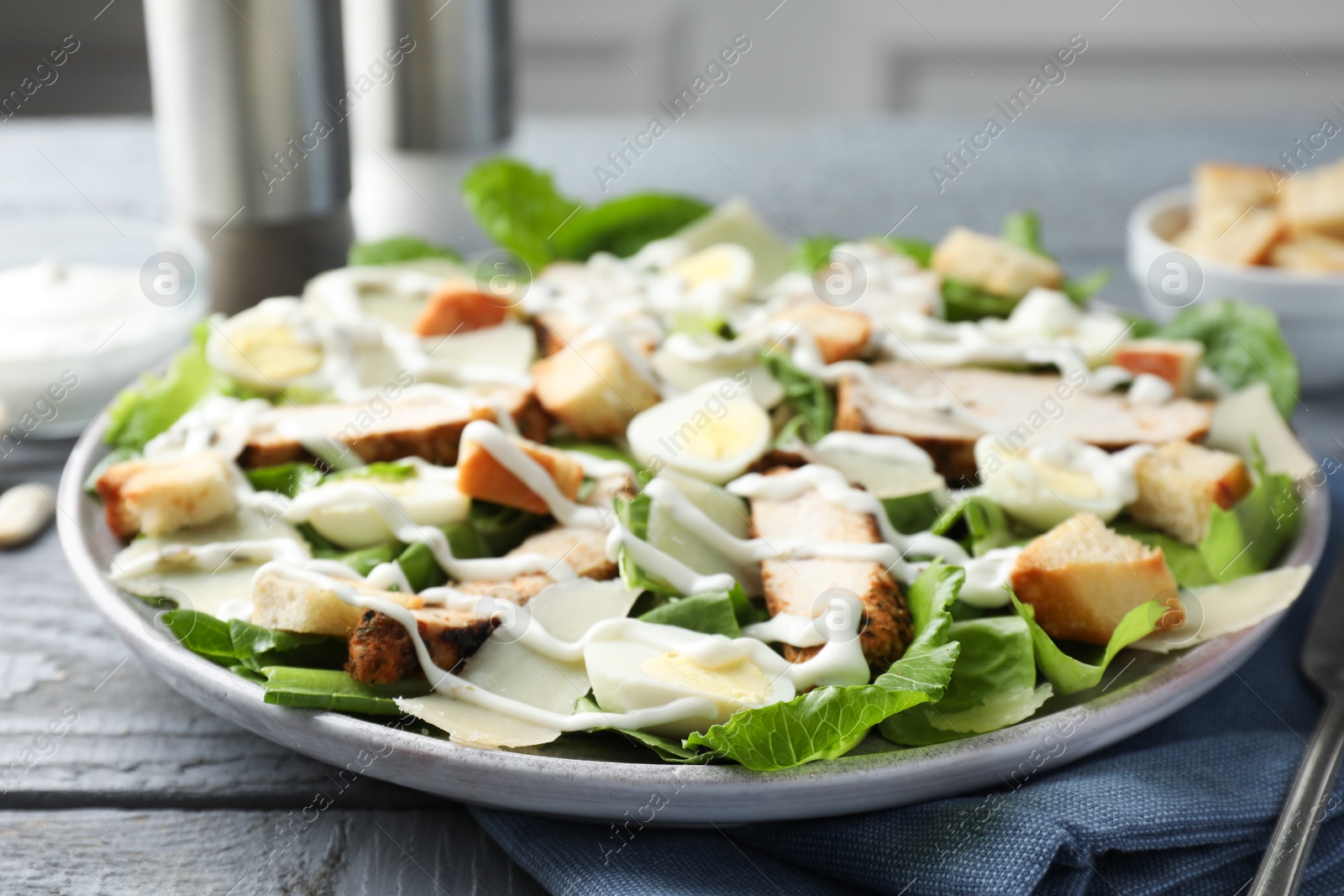 Photo of Delicious Caesar salad with chicken on grey wooden table, closeup