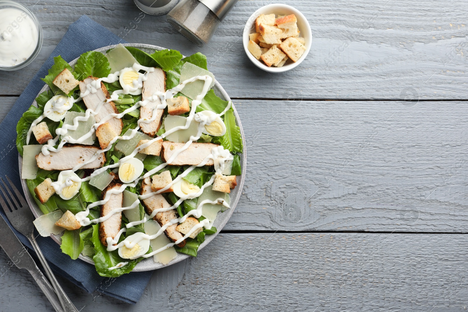 Photo of Delicious Caesar salad with chicken served on grey wooden table, flat lay. Space for text