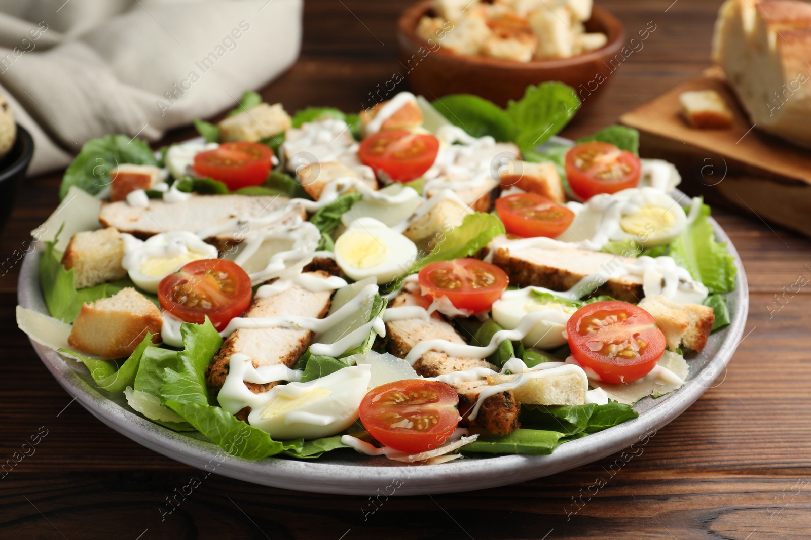 Photo of Delicious Caesar salad with chicken on wooden table, closeup