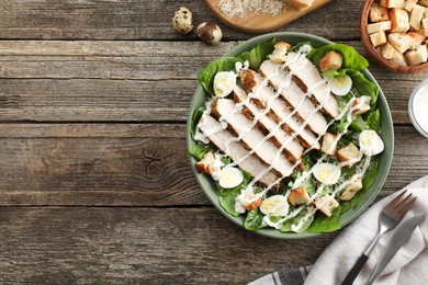 Delicious Caesar salad with chicken and other ingredients on wooden table, flat lay. Space for text