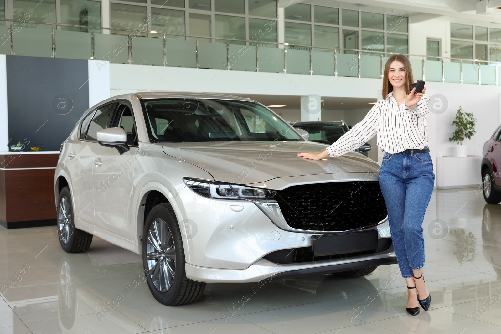 Photo of Happy young woman with key near new silver car in salon