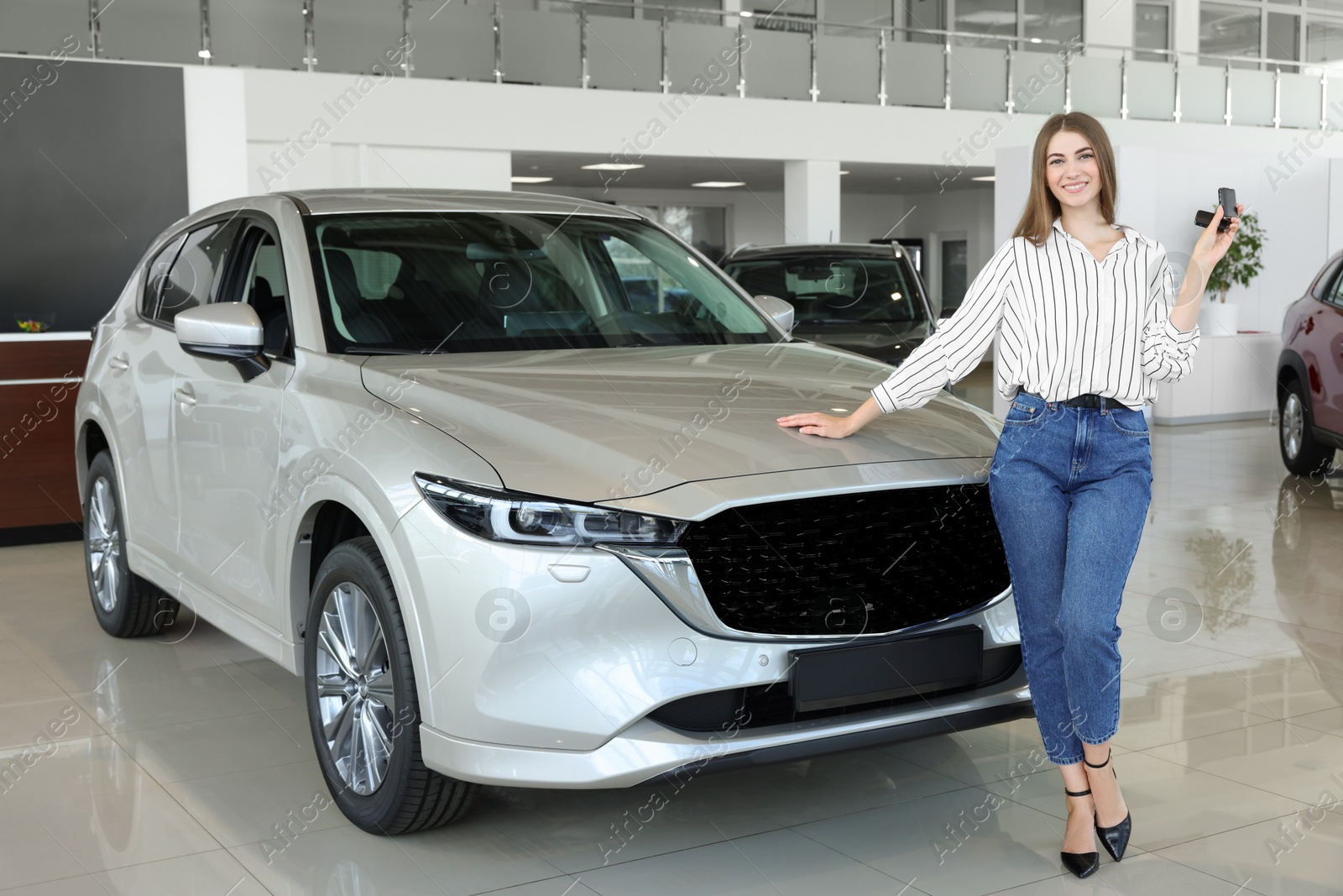 Photo of Happy young woman with key near new silver car in salon