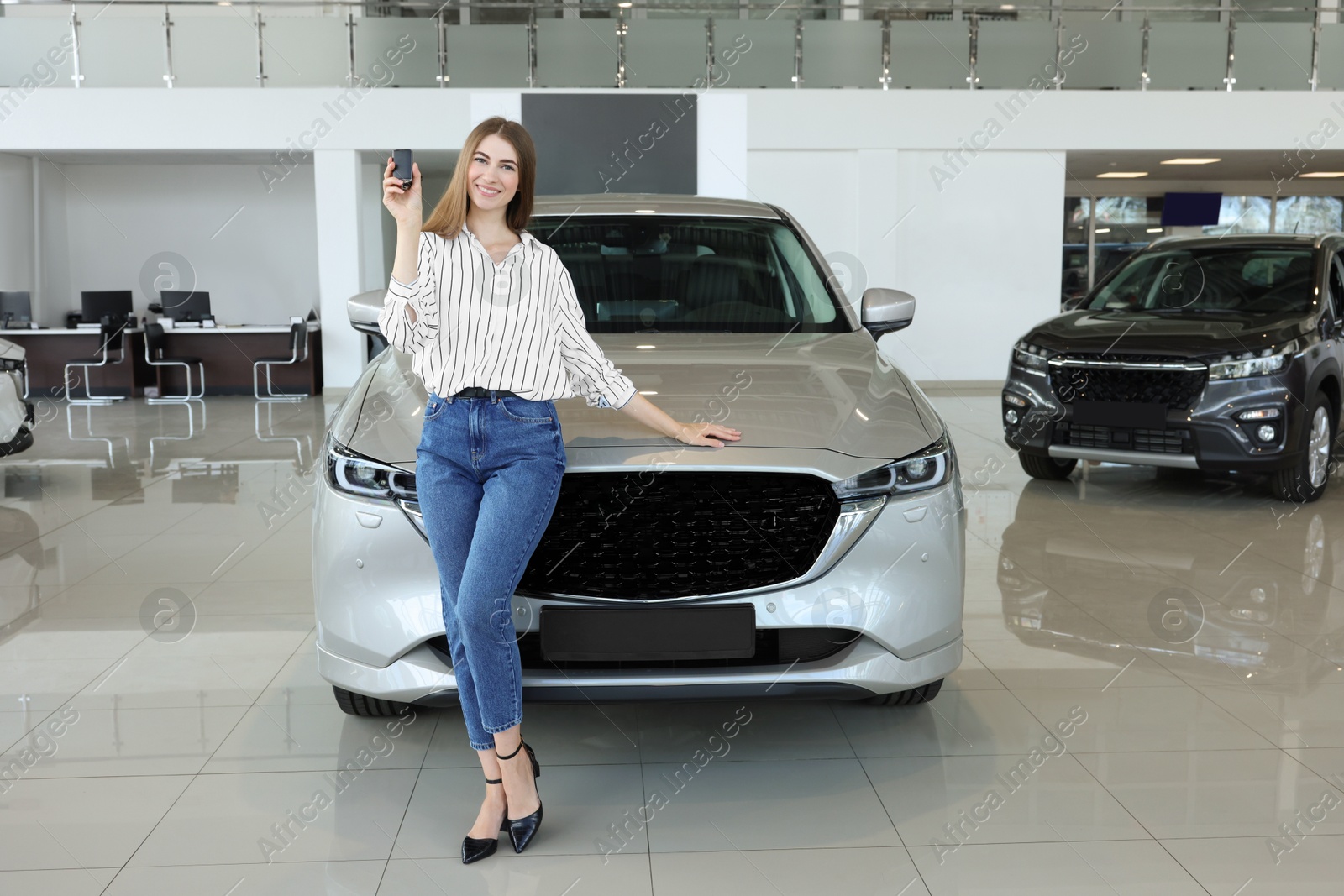 Photo of Happy young woman with key near new silver car in salon