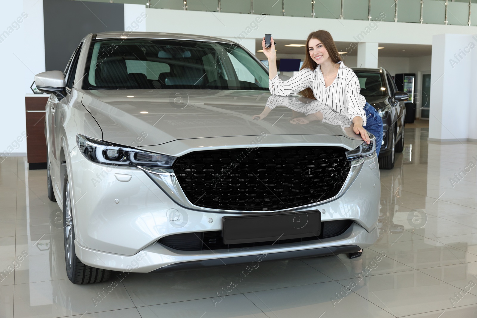 Photo of Happy young woman with key near new silver car in salon