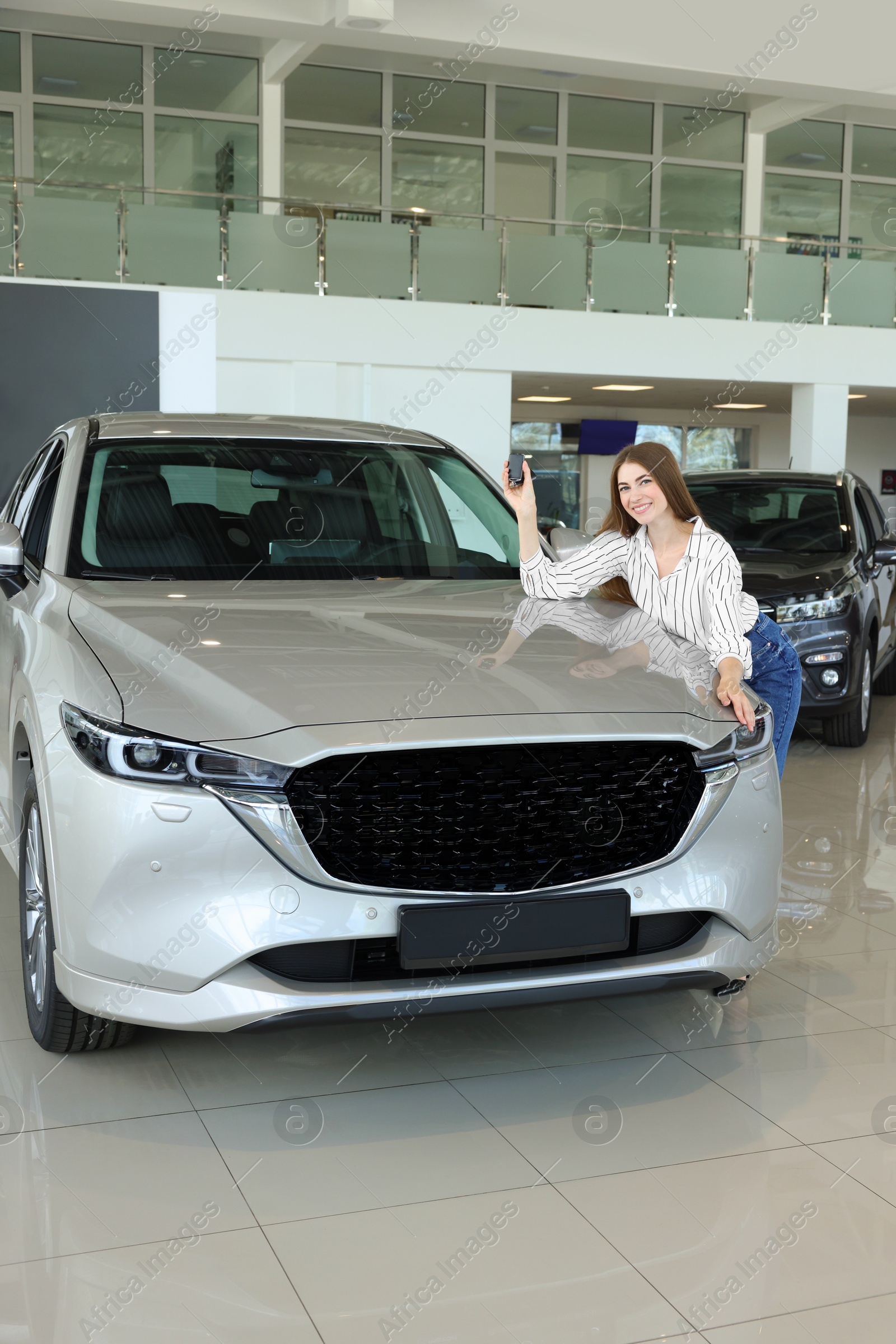 Photo of Happy young woman with key near new silver car in salon