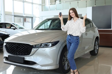 Photo of Happy young woman with key near new silver car in salon