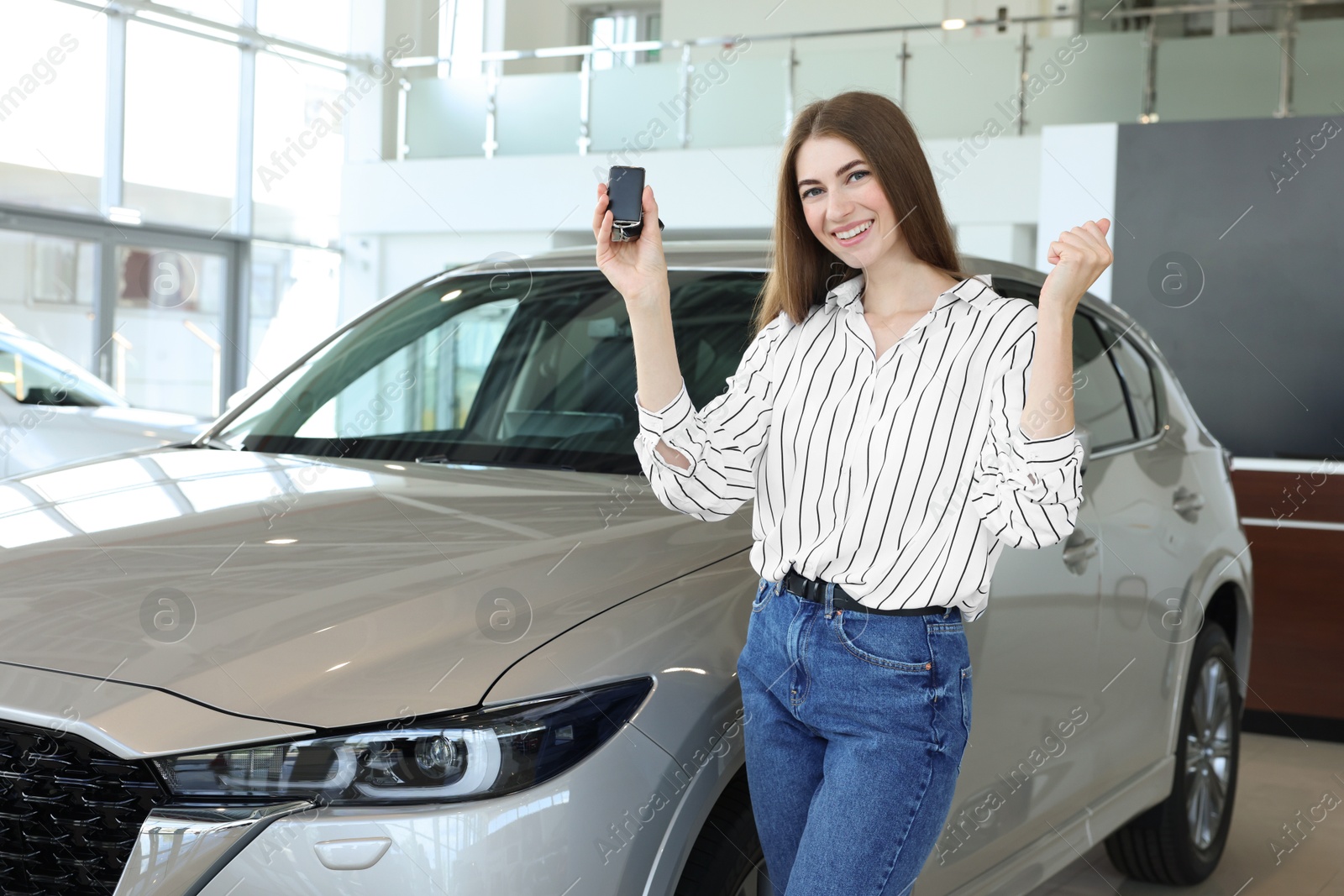 Photo of Happy young woman with key near new silver car in salon