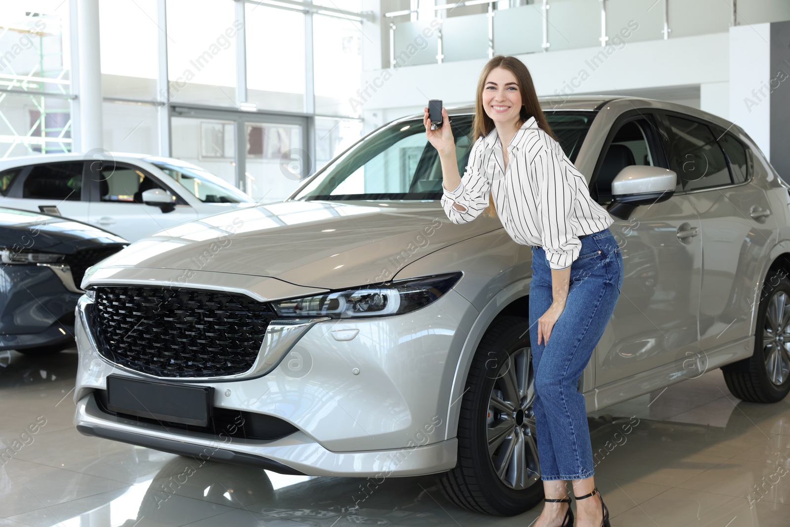 Photo of Happy young woman with key near new silver car in salon