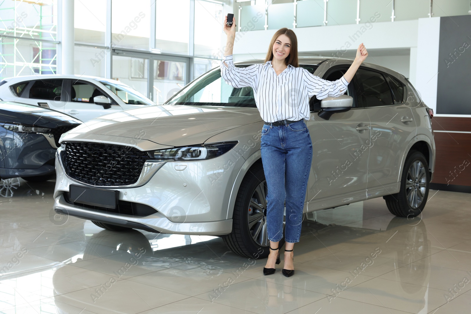 Photo of Happy young woman with key near new silver car in salon