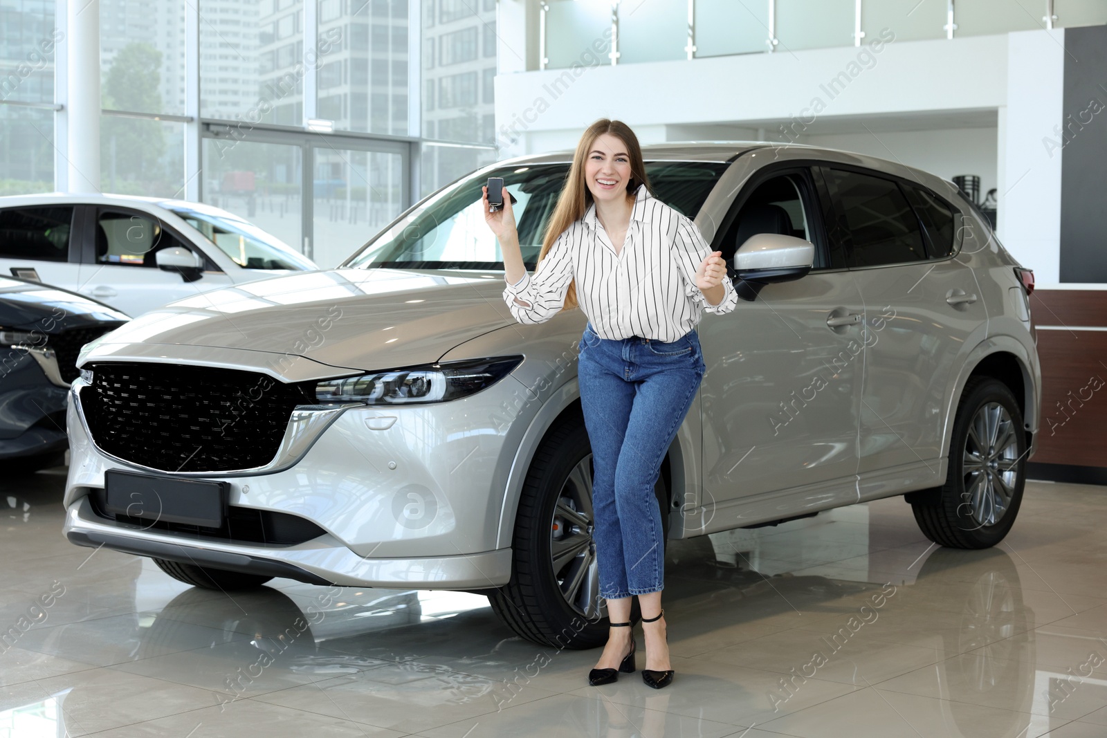 Photo of Happy young woman with key near new silver car in salon