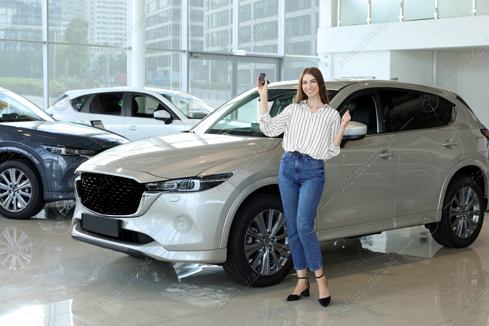 Photo of Happy young woman with key near new silver car in salon