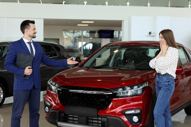 Photo of Salesman and client near new red car in salon