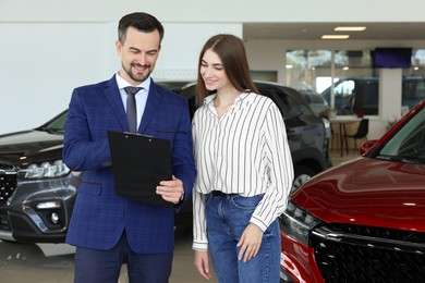 Photo of Salesman and client near new red car in salon