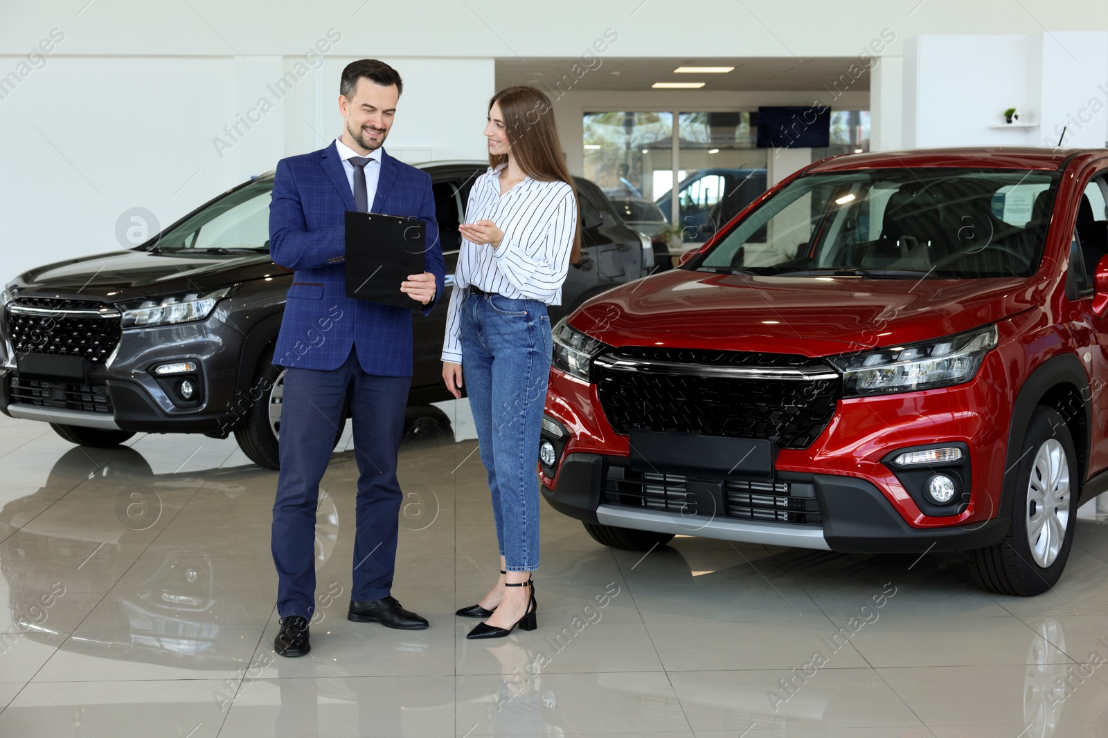 Photo of Salesman and client near new red car in salon