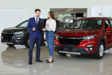 Photo of Salesman and client near new red car in salon