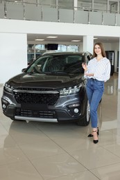 Photo of Happy young woman holding key near new black car in salon