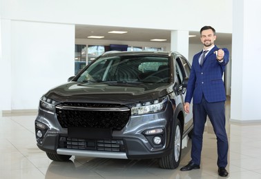 Photo of Happy salesman holding key near new black car in salon