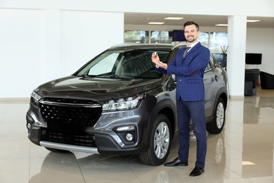 Photo of Happy salesman holding key near new black car in salon