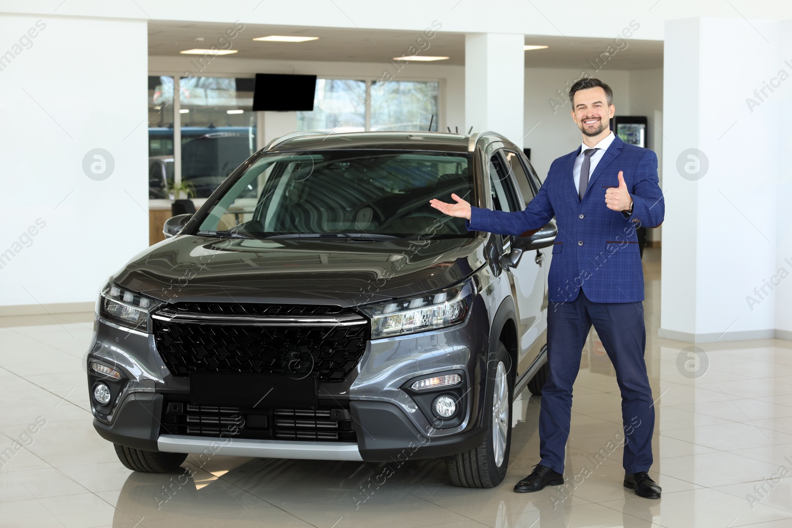 Photo of Happy salesman showing thumbs up near new black car in salon