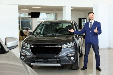 Photo of Happy salesman showing thumbs up near new black car in salon