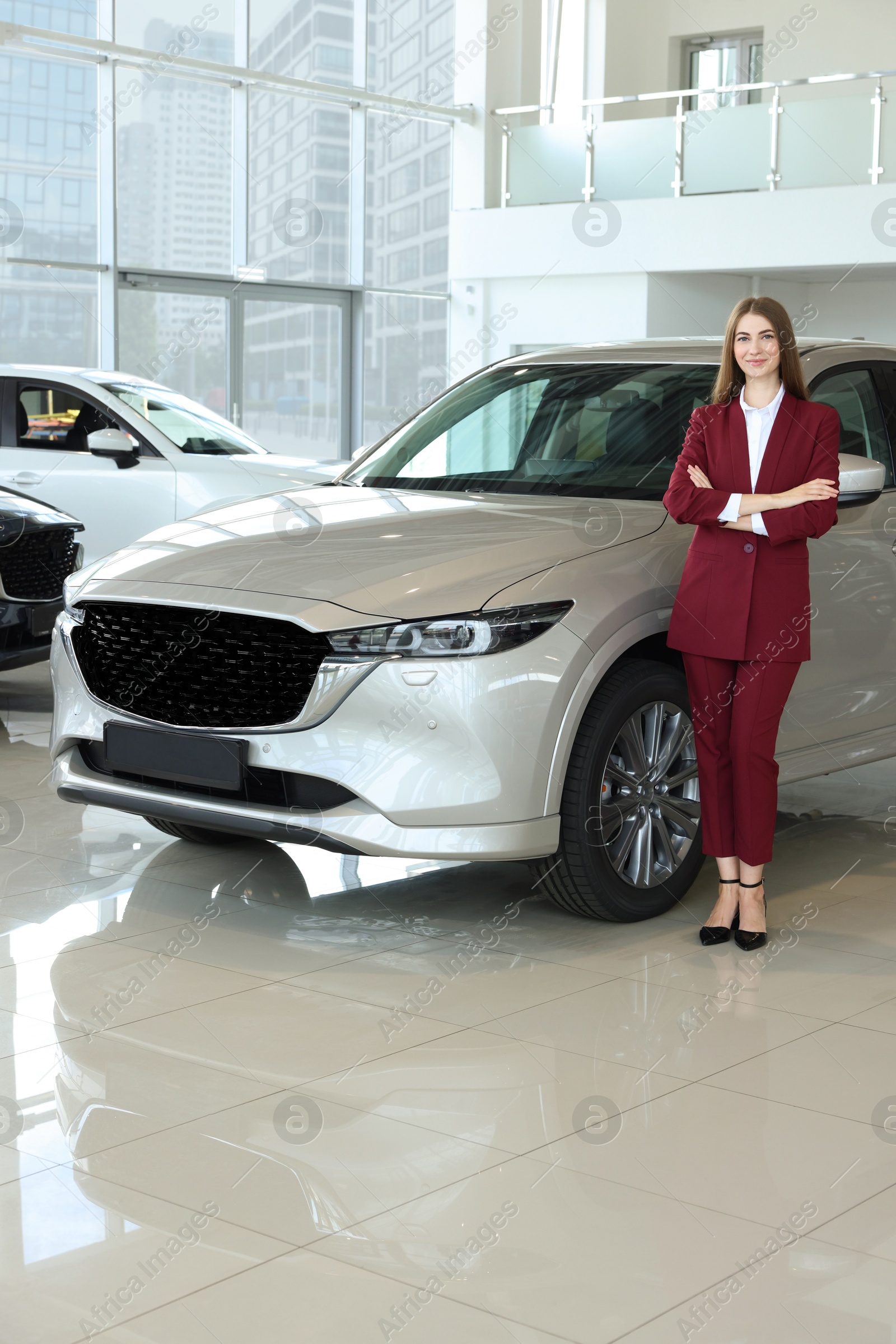 Photo of Happy saleswoman near new silver car in salon