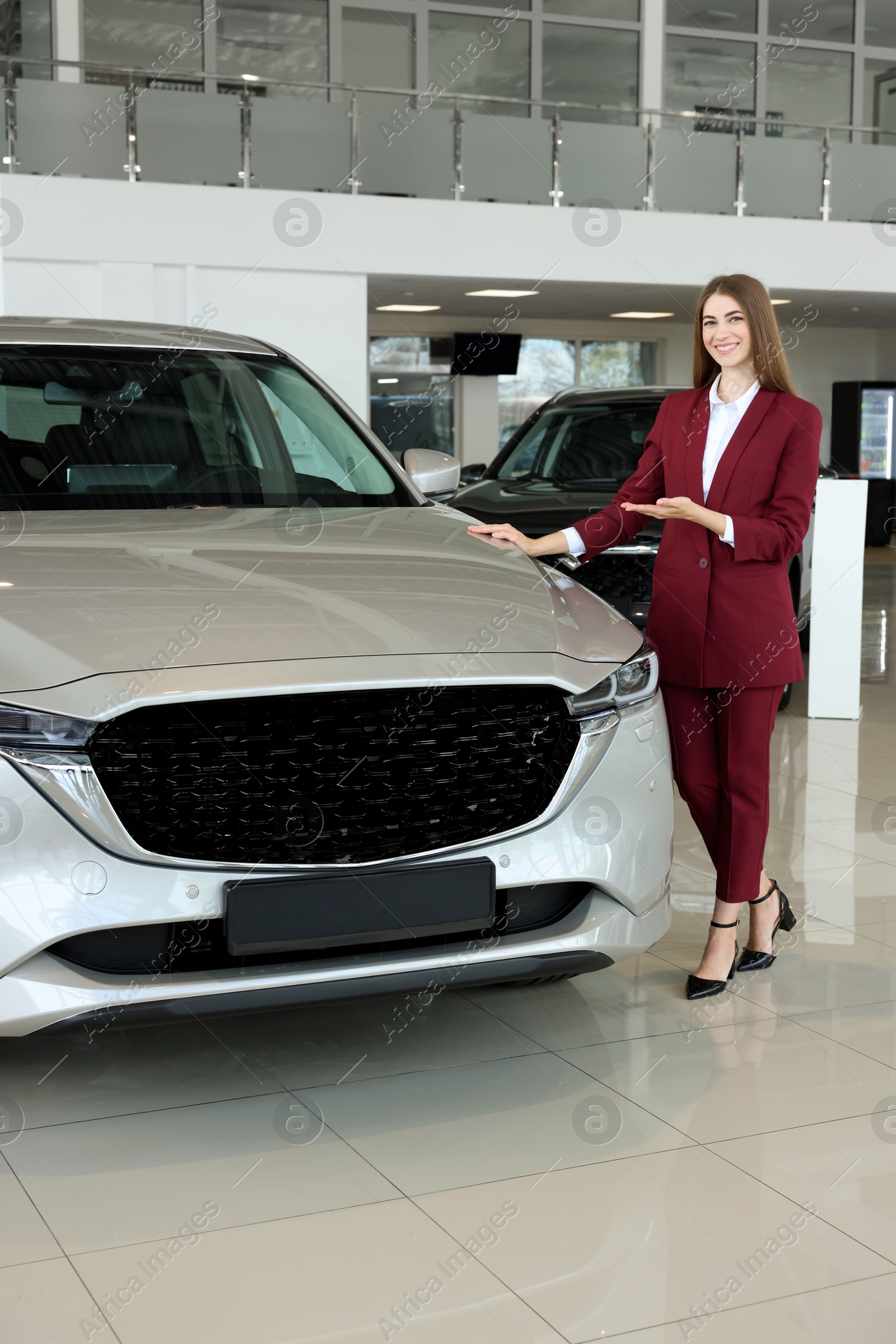 Photo of Happy saleswoman near new silver car in salon