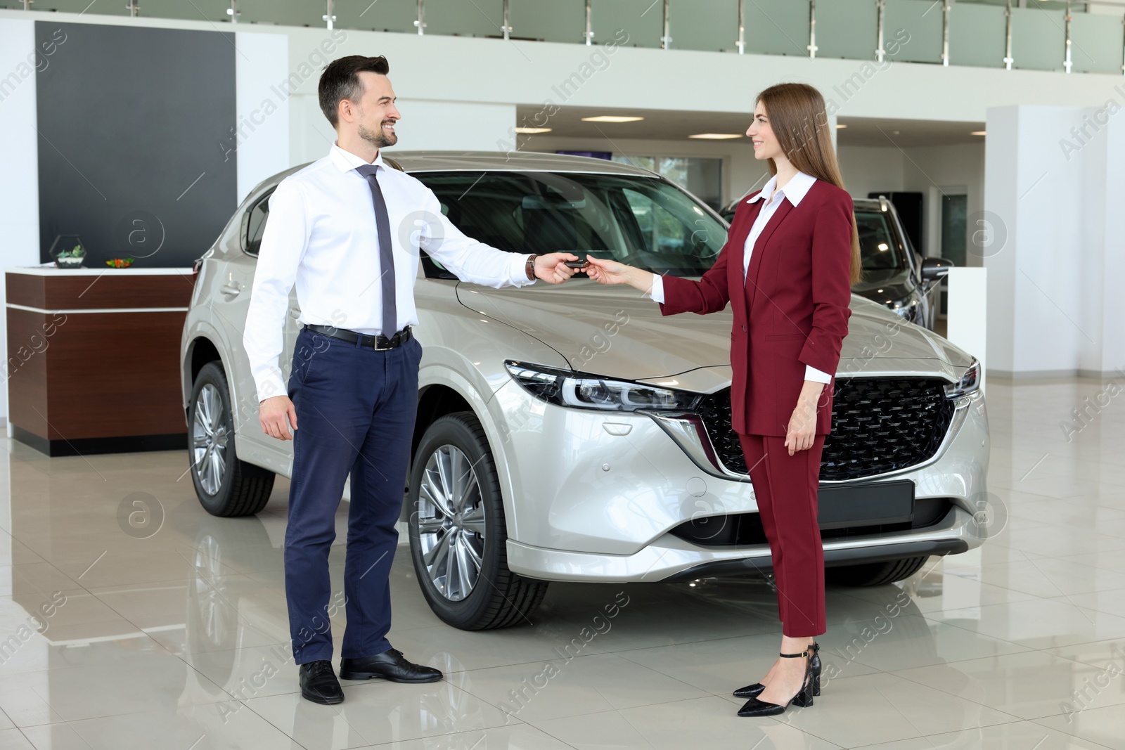 Photo of Salesman giving key to client near new car in salon