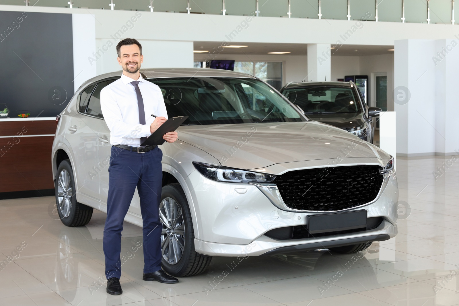 Photo of Happy salesman near new silver car in salon