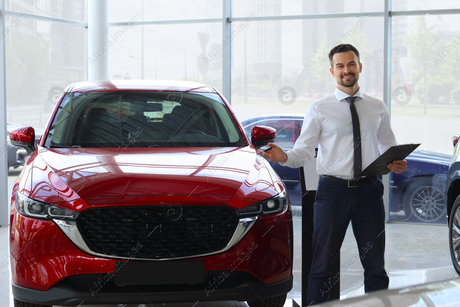 Photo of Happy salesman near new red car in salon