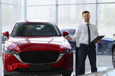 Photo of Happy salesman near new red car in salon