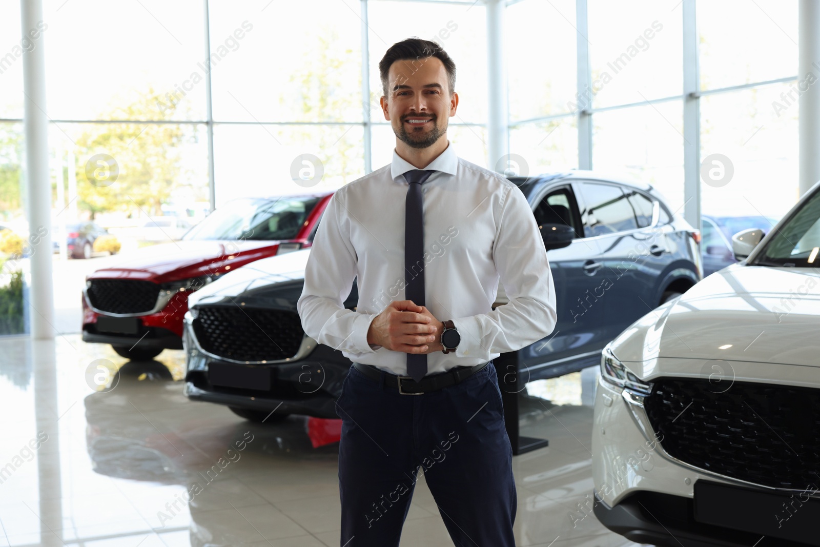 Photo of Happy salesman near new cars in salon