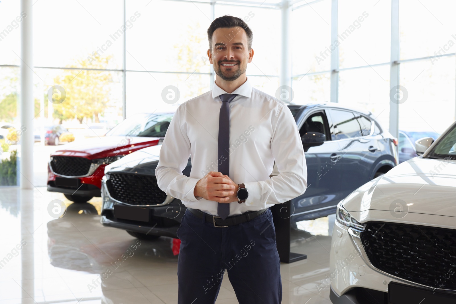 Photo of Happy salesman near new cars in salon