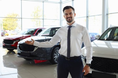 Photo of Happy salesman near new cars in salon