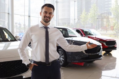 Photo of Happy salesman near new cars in salon