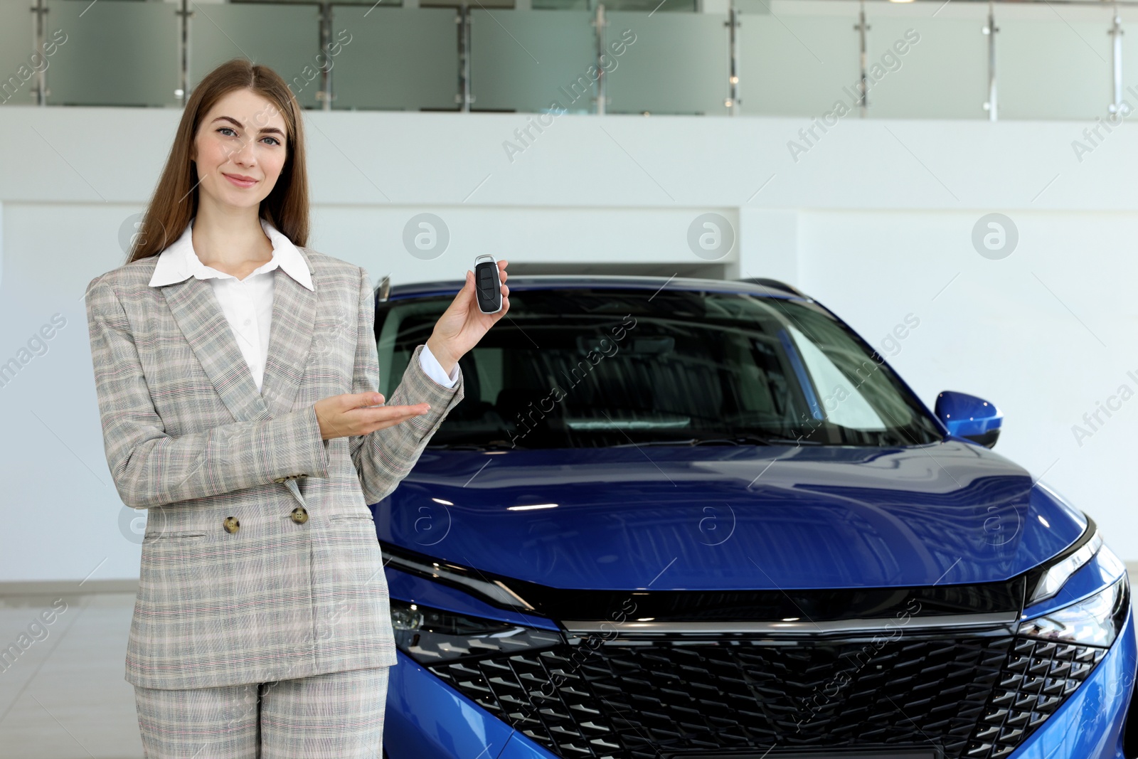 Photo of Happy saleswoman holding key near new car in salon