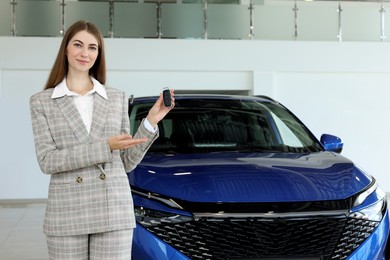 Photo of Happy saleswoman holding key near new car in salon