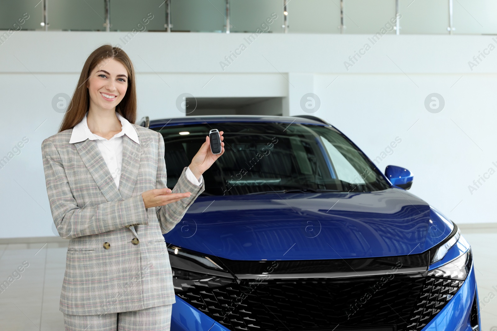 Photo of Happy saleswoman holding key near new car in salon