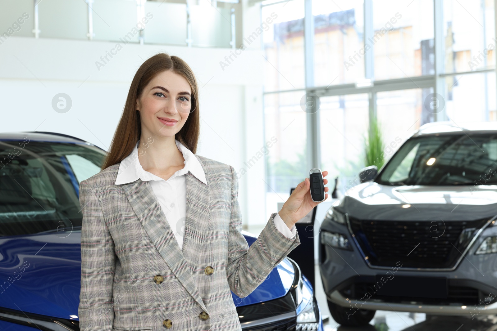 Photo of Happy saleswoman holding key near new car in salon