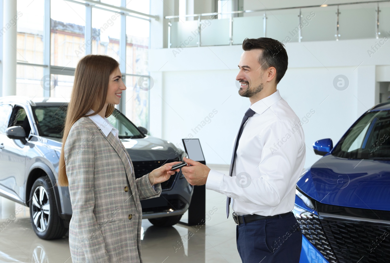 Photo of Saleswoman giving key to client near new car in salon