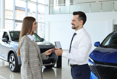 Photo of Saleswoman giving key to client near new car in salon