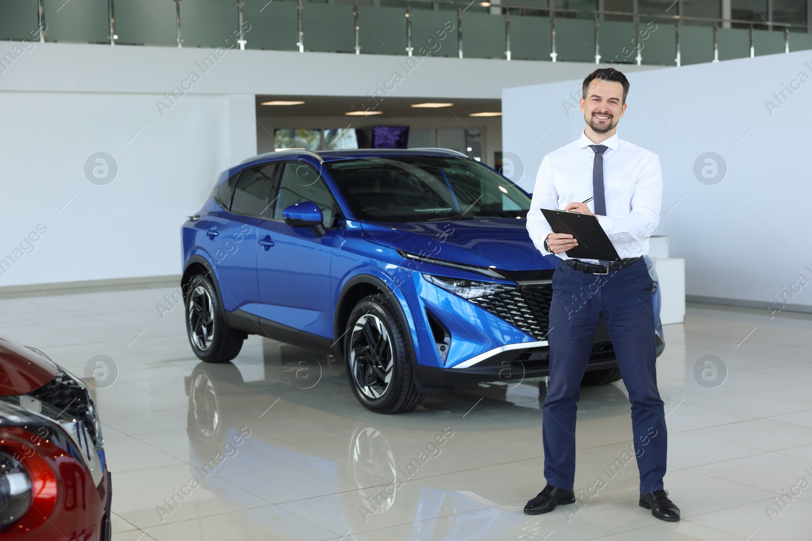 Photo of Happy salesman near new blue car in salon