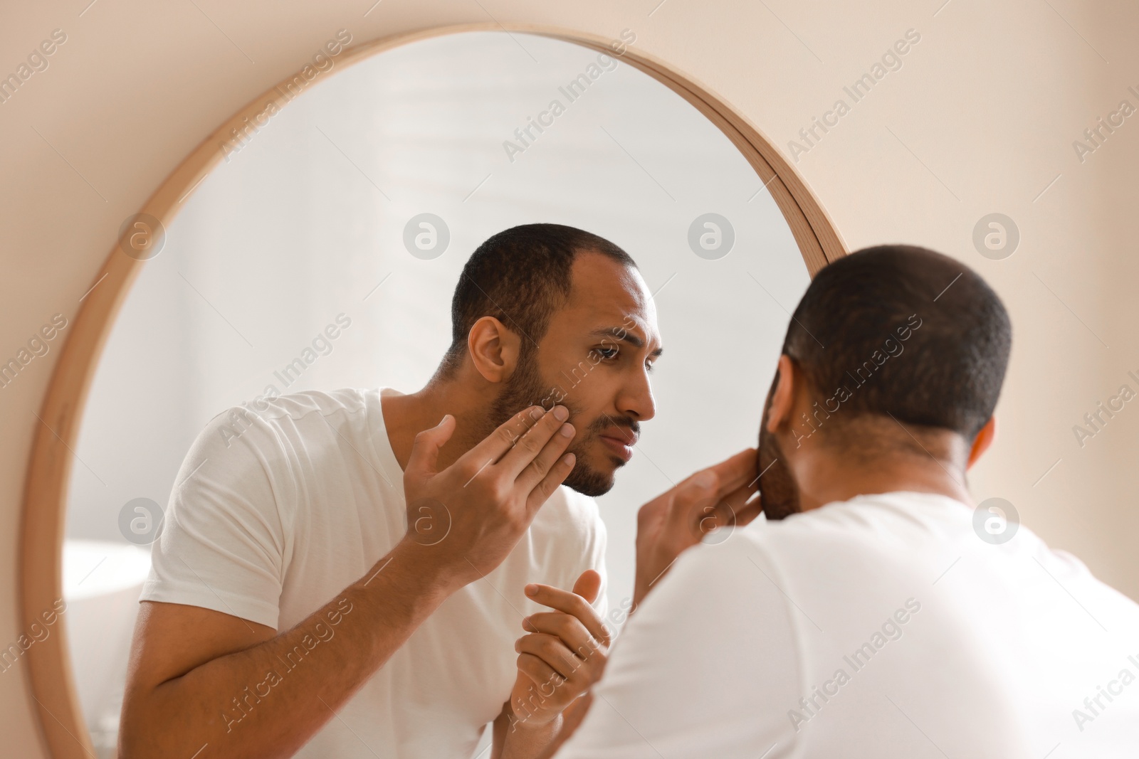 Photo of Worried man looking at mirror in bathroom