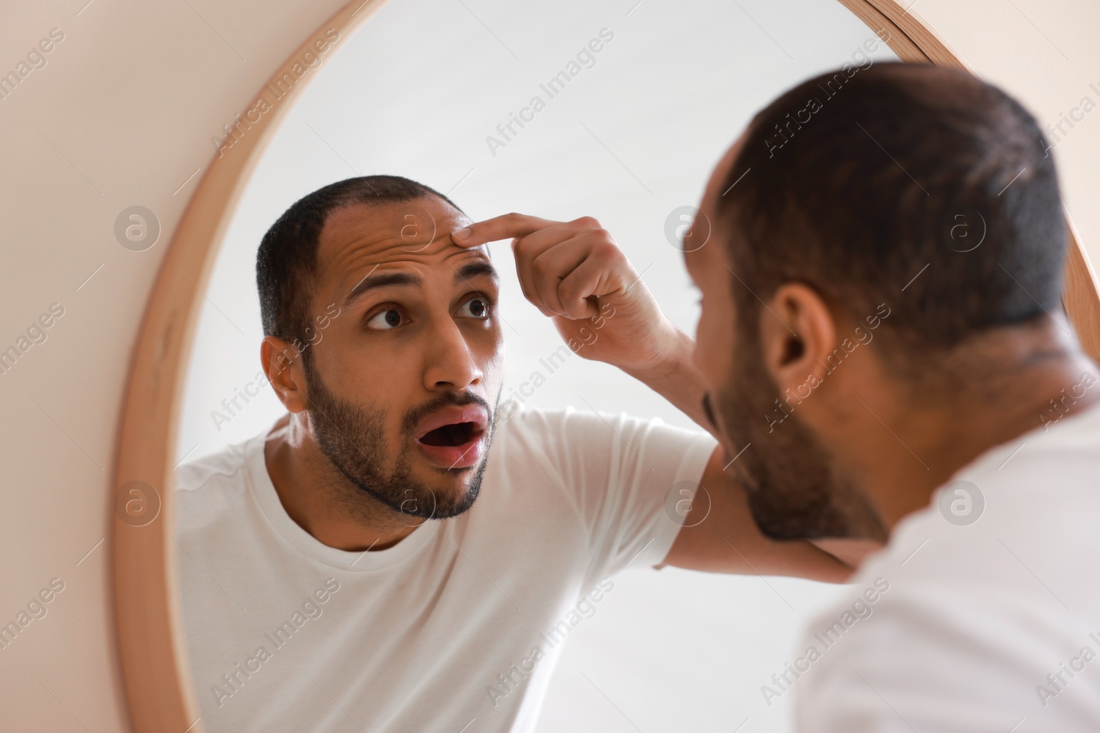 Photo of Worried man looking at mirror in bathroom