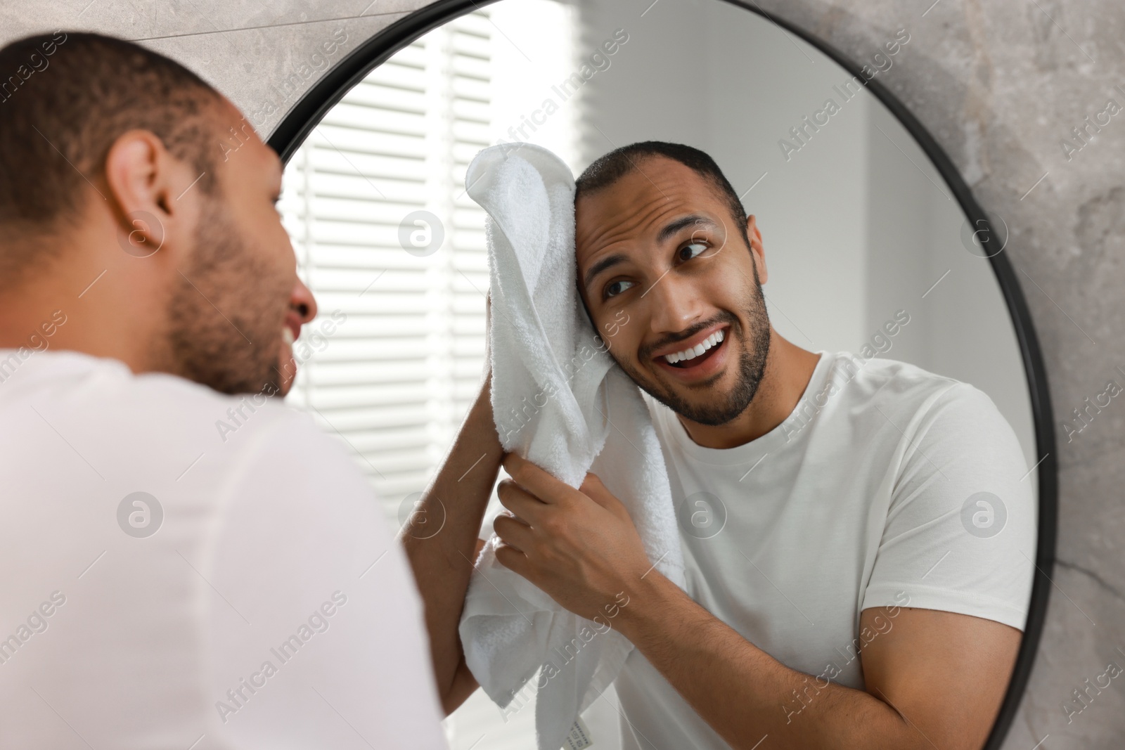 Photo of Smiling man with towel looking at mirror in bathroom