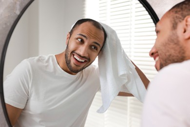 Photo of Smiling man with towel looking at mirror in bathroom