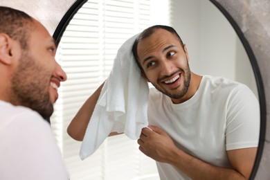 Photo of Smiling man with towel looking at mirror in bathroom